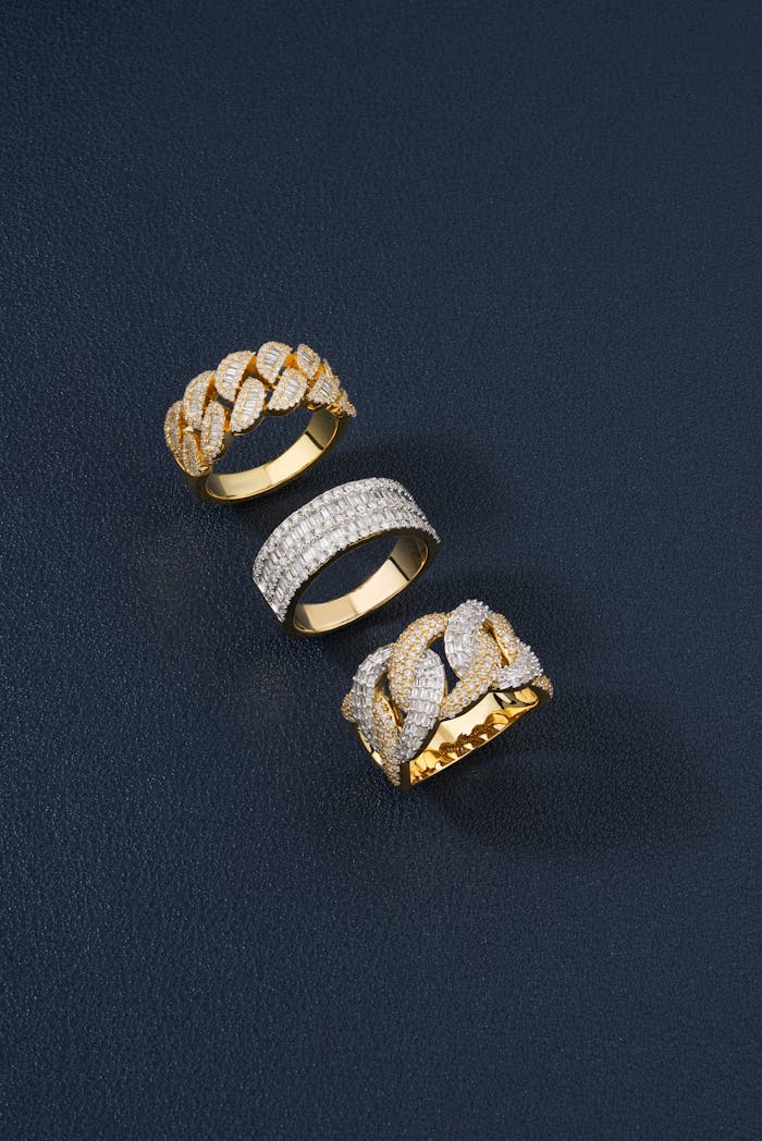 Three elegant golden rings with diamonds against a dark textured surface, showcasing luxury and style.