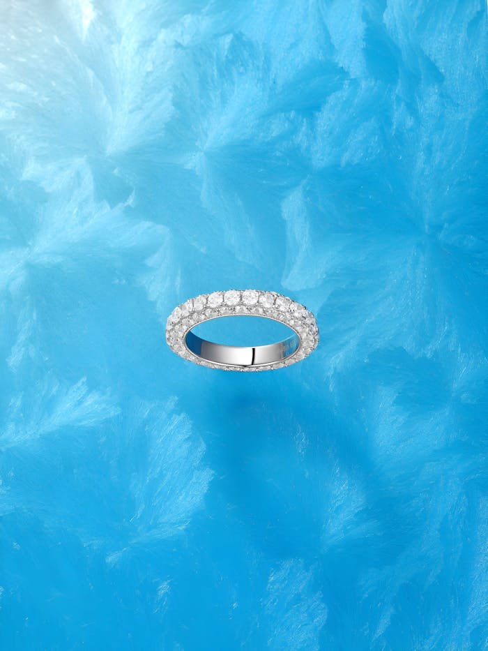 Elegant diamond eternity ring on an artistic blue background, showcasing luxury jewelry design.